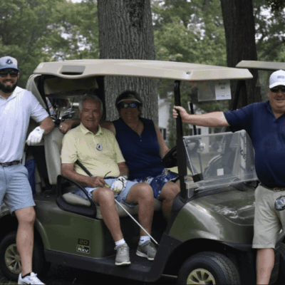 Four men enjoying a golf outing with a golf cart in a lush green setting.